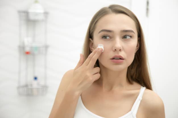 young-beautiful-woman-applying-cream-to-face-in-the-bathroom_1163-2272.jpg